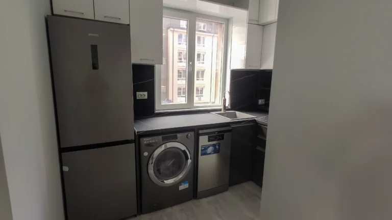 Компактна кухня с всички уреди по ред – хладилник, пералня, съдомиялна, мивка.