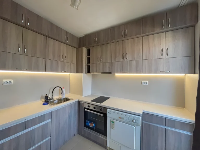 Пълен изглед на кухнята – осветена композиция в дървесни тонове и светъл плот Шампейн.